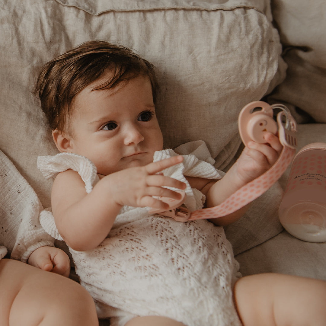 Baby holding a pink Suavinex Bonhomia Owl soother attached to its soother chain