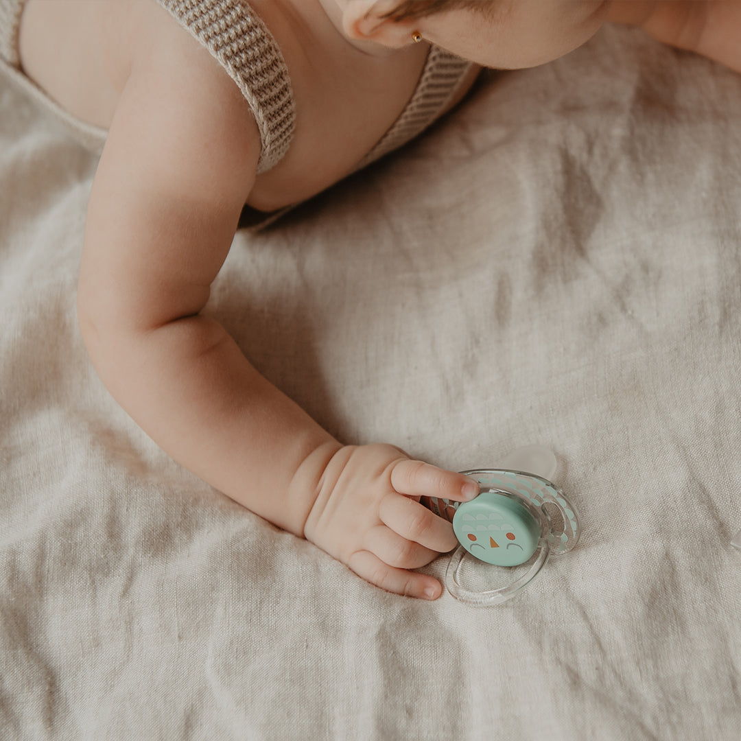 Close up of a baby reaching for a Suavinex Bonhomia Owl soother on a linen sheet