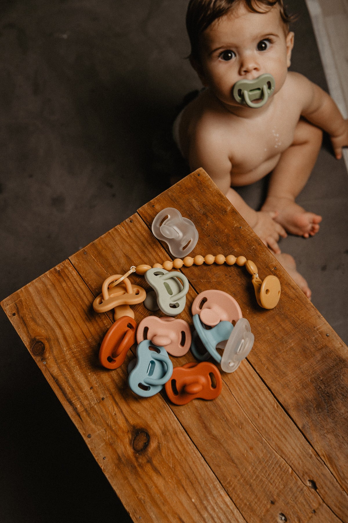 Flat lay of Suavinex Colour Essence soothers, clip and case in a range of colours